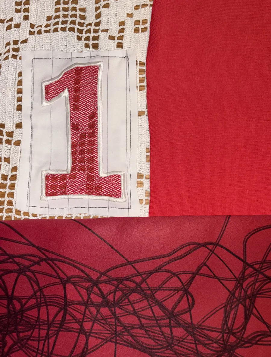 Number 1 stitched onto lace, red fabric and loose black threads.
