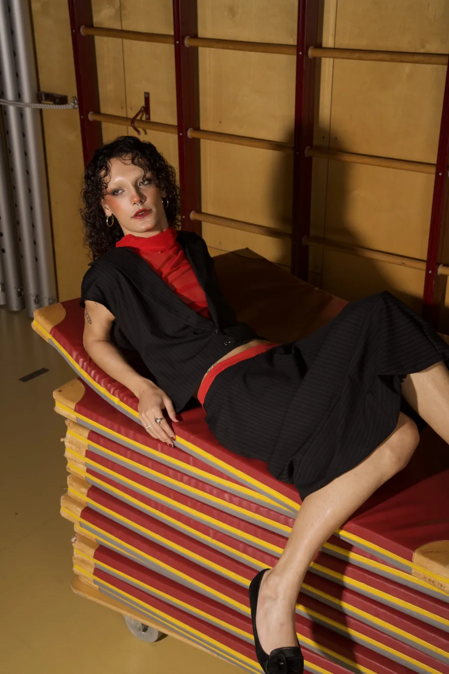 Model in the black vest and skirt reclining on stacked gym mats.