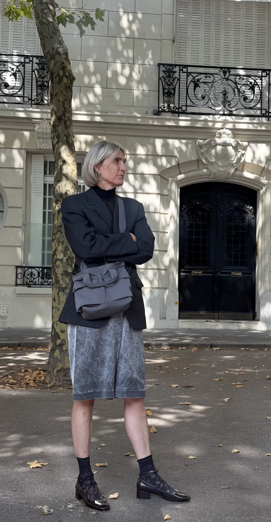 Woman with grey hair in a black blazer and grey skirt in front of a classic facade.