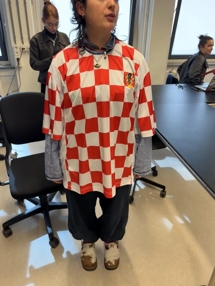 Person in a red and white checked football shirt over a striped shirt and wide trousers.
