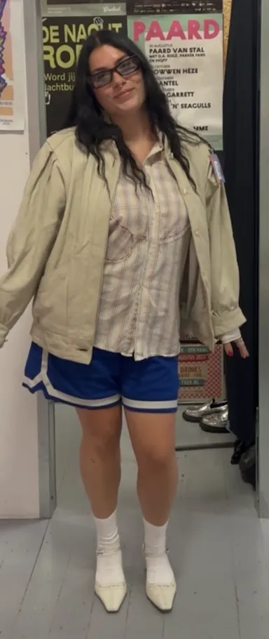 Person in a beige bomber, striped shirt and blue basketball shorts with white socks.