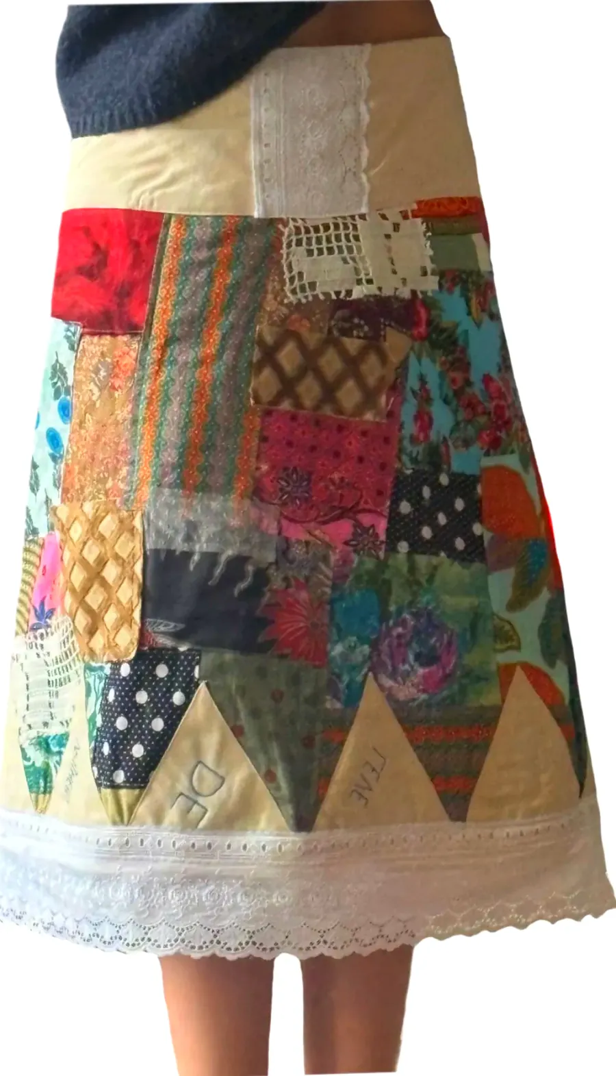 The patchwork skirt worn, seen from the side: a cream waistband, colourful patches and a row of triangles above a lace hem.